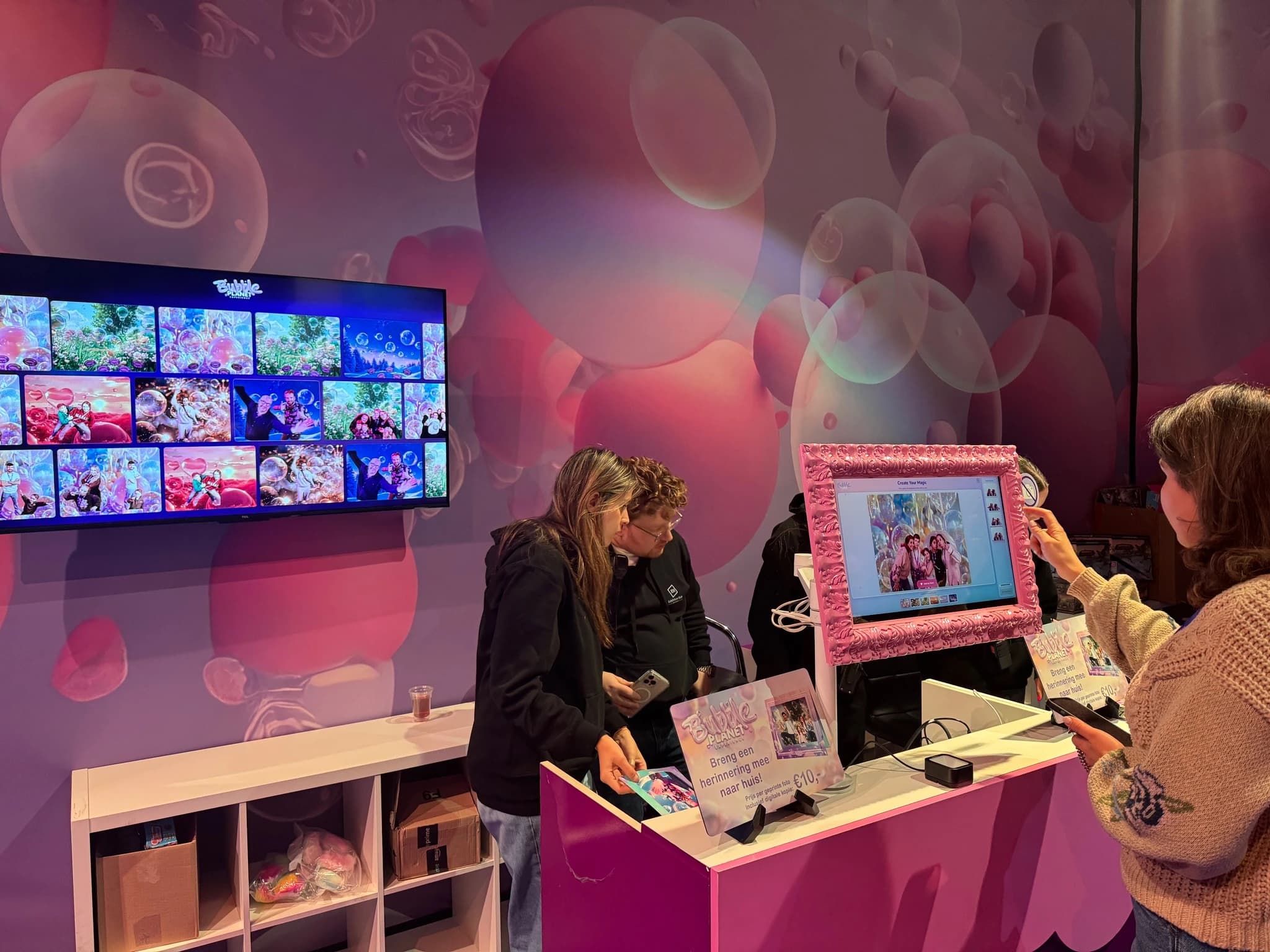 Guests reviewing and collecting photos at the Bubble Planet shop counter, under a wall screen of recent groups